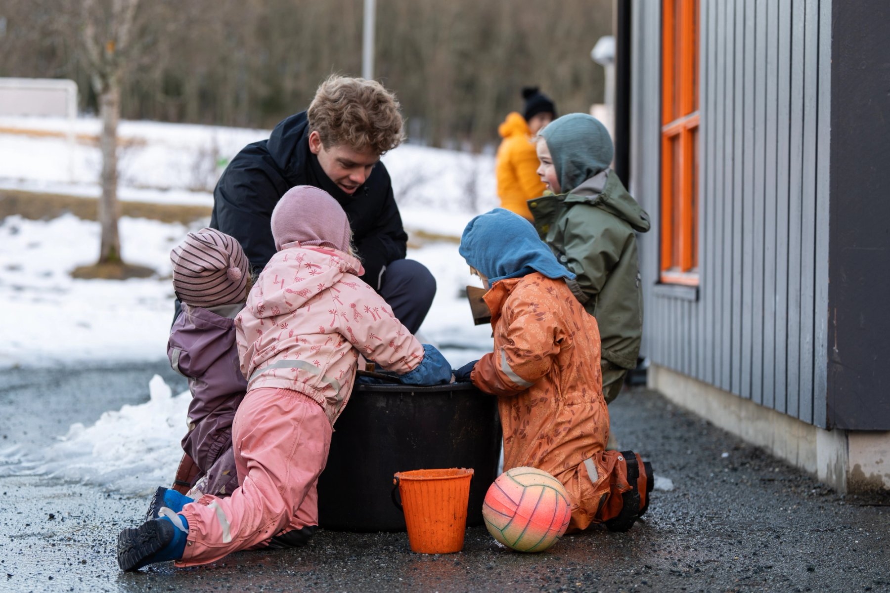 Foto av fire barn som utforsker en bøtte med vann sammen med barnehageansatt. 