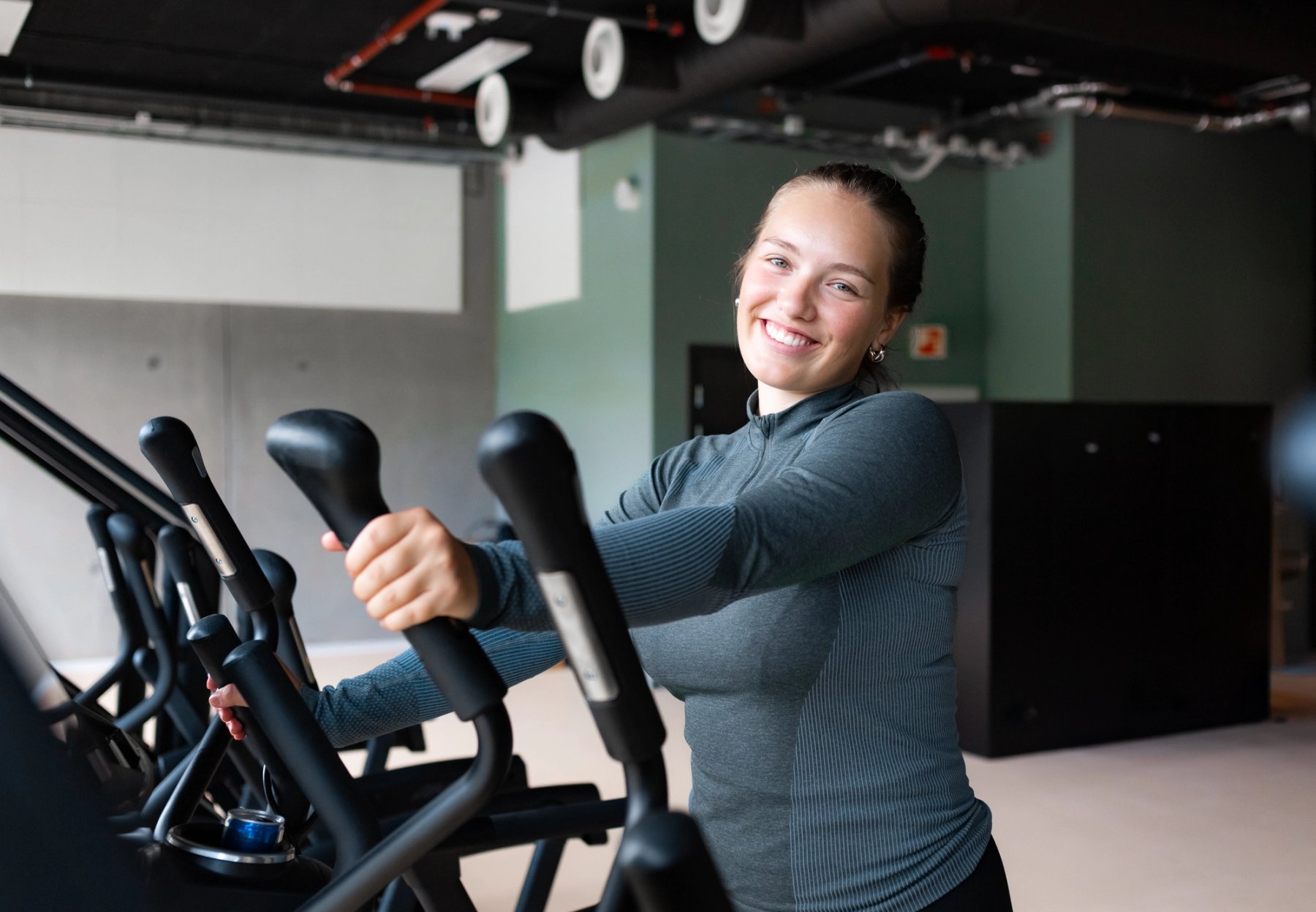 A smiling student working out on an elliptical machine at a Sit gym.