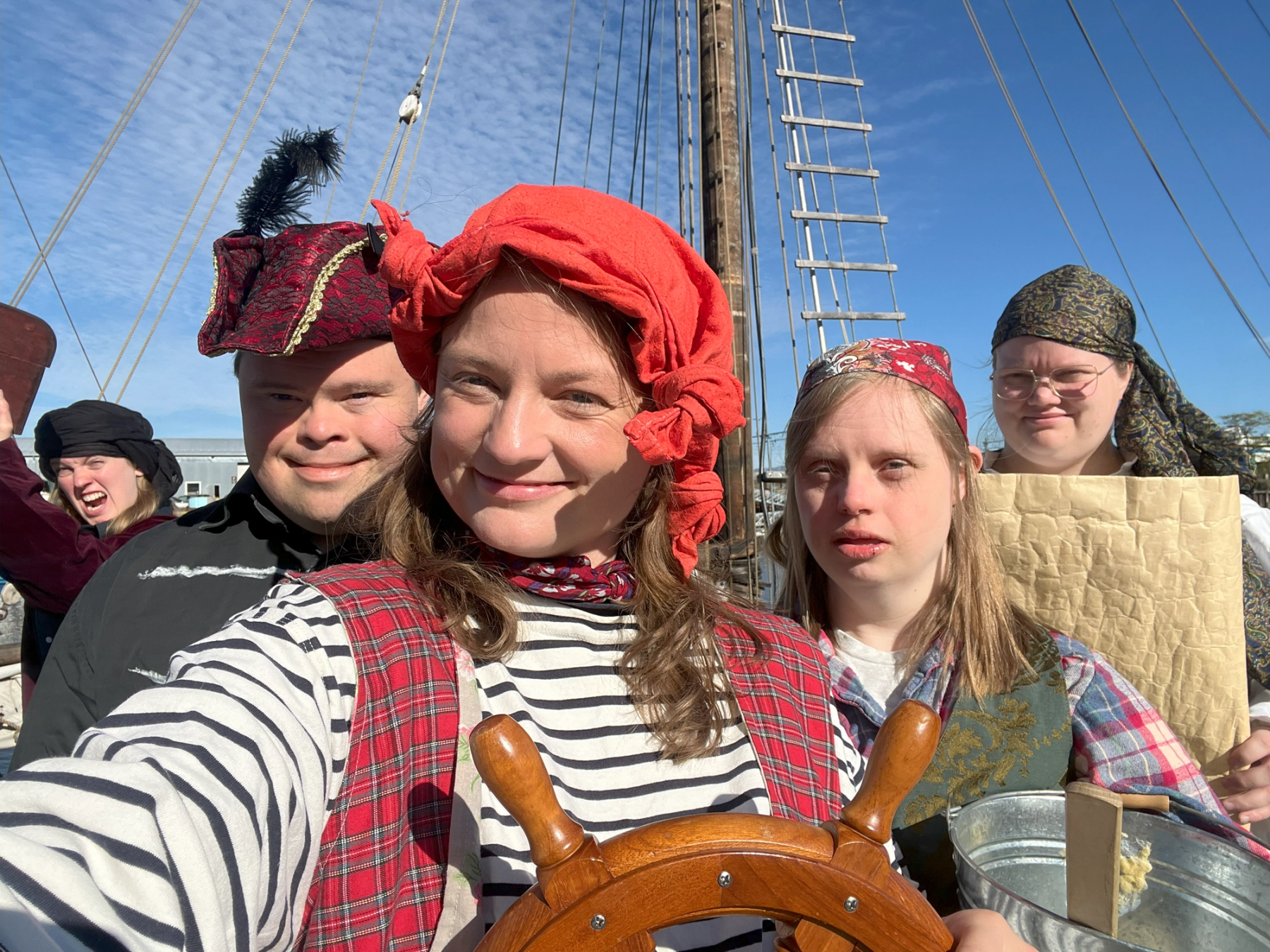 En gruppe glade skuespillere utkledd som sjørøvere står på dekk av et skip. Alle har fargerike kostymer og hodeplagg, klare for sjørøverforestilling.