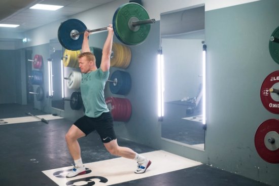 En sterk mann med splittet beinstilling som presser en vektstang over hodet.