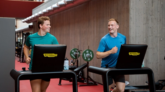 To gutter på hver sin tredemølle som ser på hverandre og smiler. 