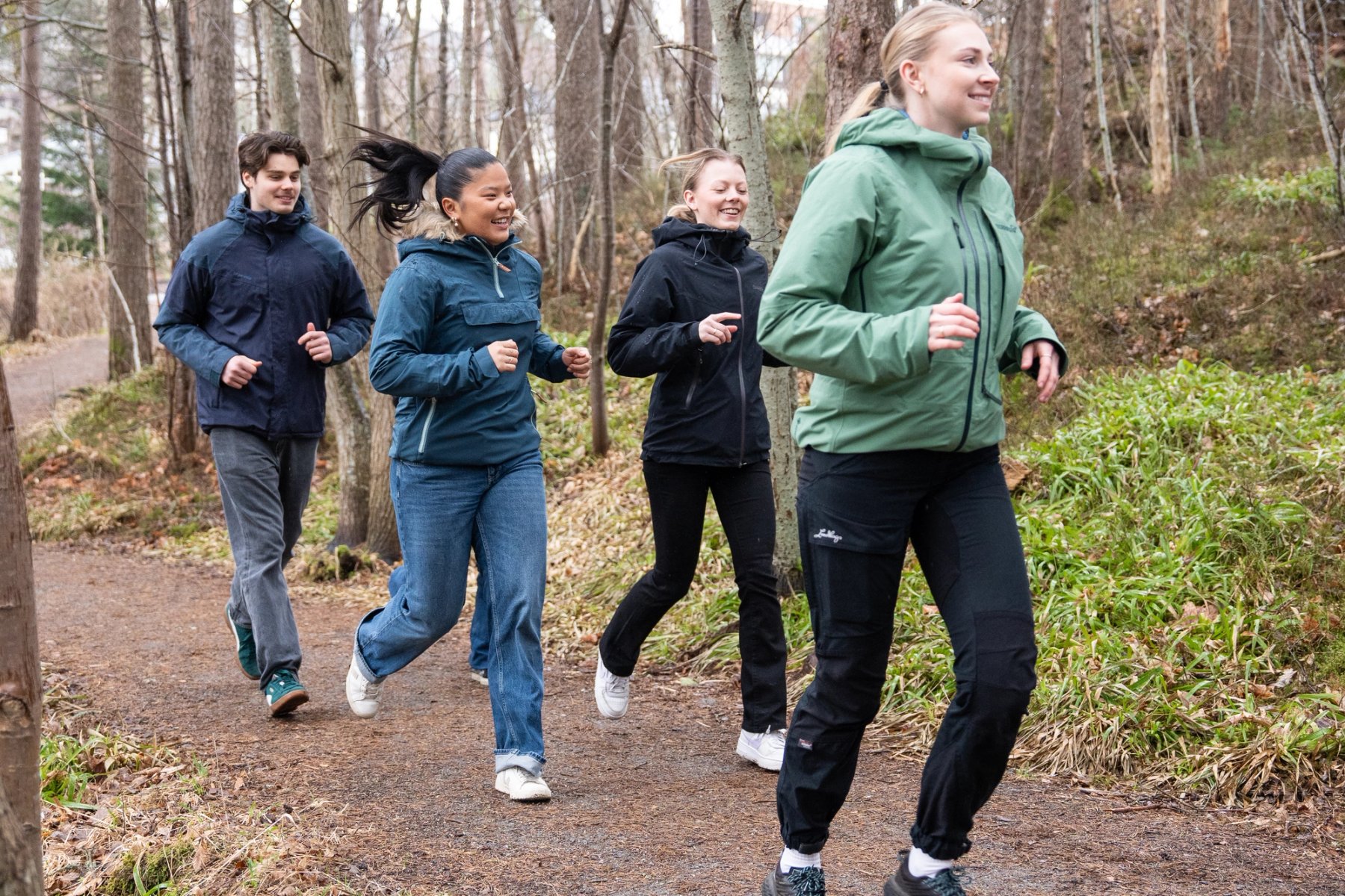 Fire studenter smiler og løper sammen gjennom skogen