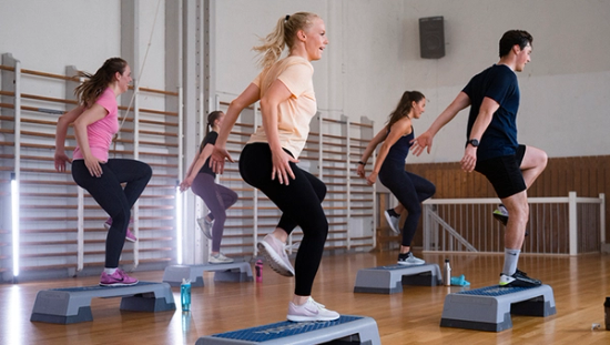 Fem personer som trener med step; de har ett ben på stepkassen og andre kneet løftet. 
