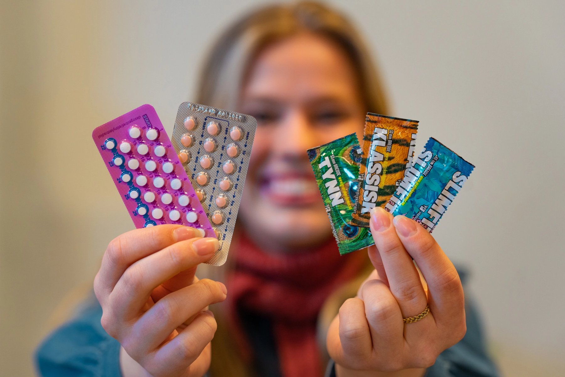 Image of a person holding birth control pills and condoms in their hand, with a smile in the background.