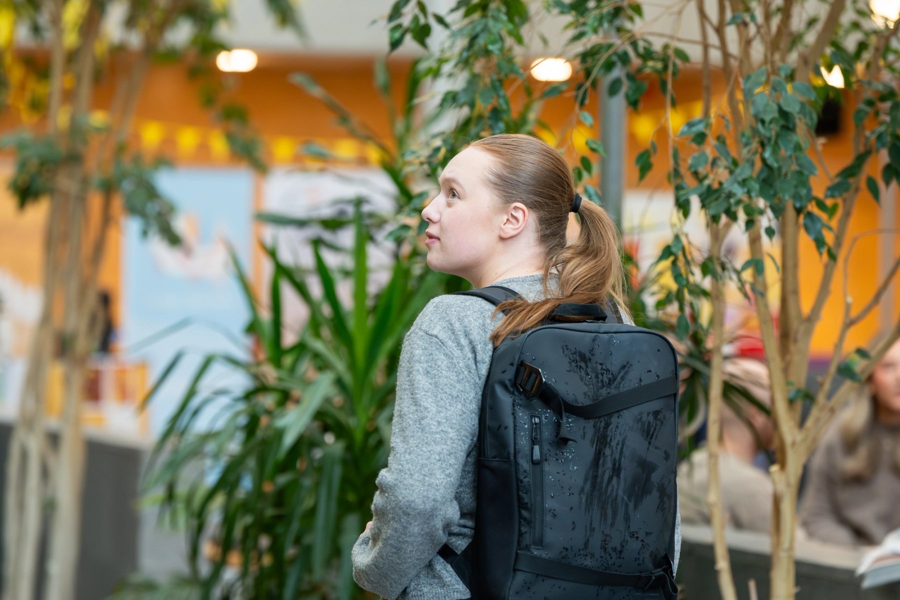 Student med ryggsekk går gjennom et lyst innendørsområde med grønne planter i et NTNU-bygg.