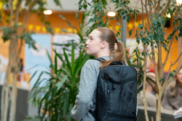 En kvinnelig student ser litt alene ut og ser seg rundt på campus. Hun har på seg en skolesekk på ryggen.