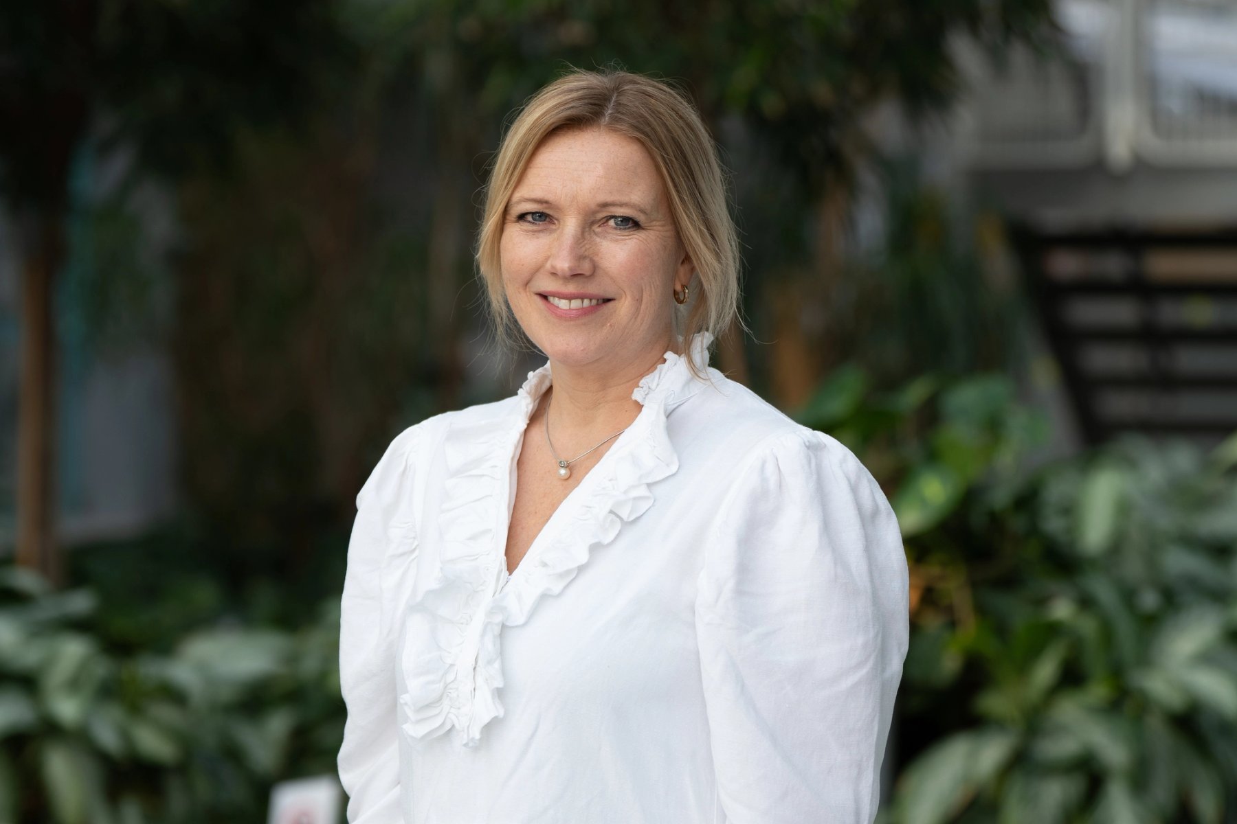 Bente Haldorsen, ansattrepresentant, Sit, smiler mot kamera i et grønt utemiljø.