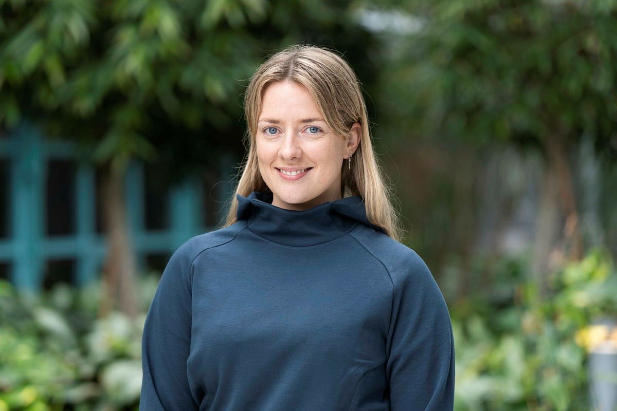 Portrett av Svala Eyjolfsdottir, prosjektleder og treningsinstruktør i Sit Trondheim. Hun smiler mot kamera og står utenfor et grønt miljø.