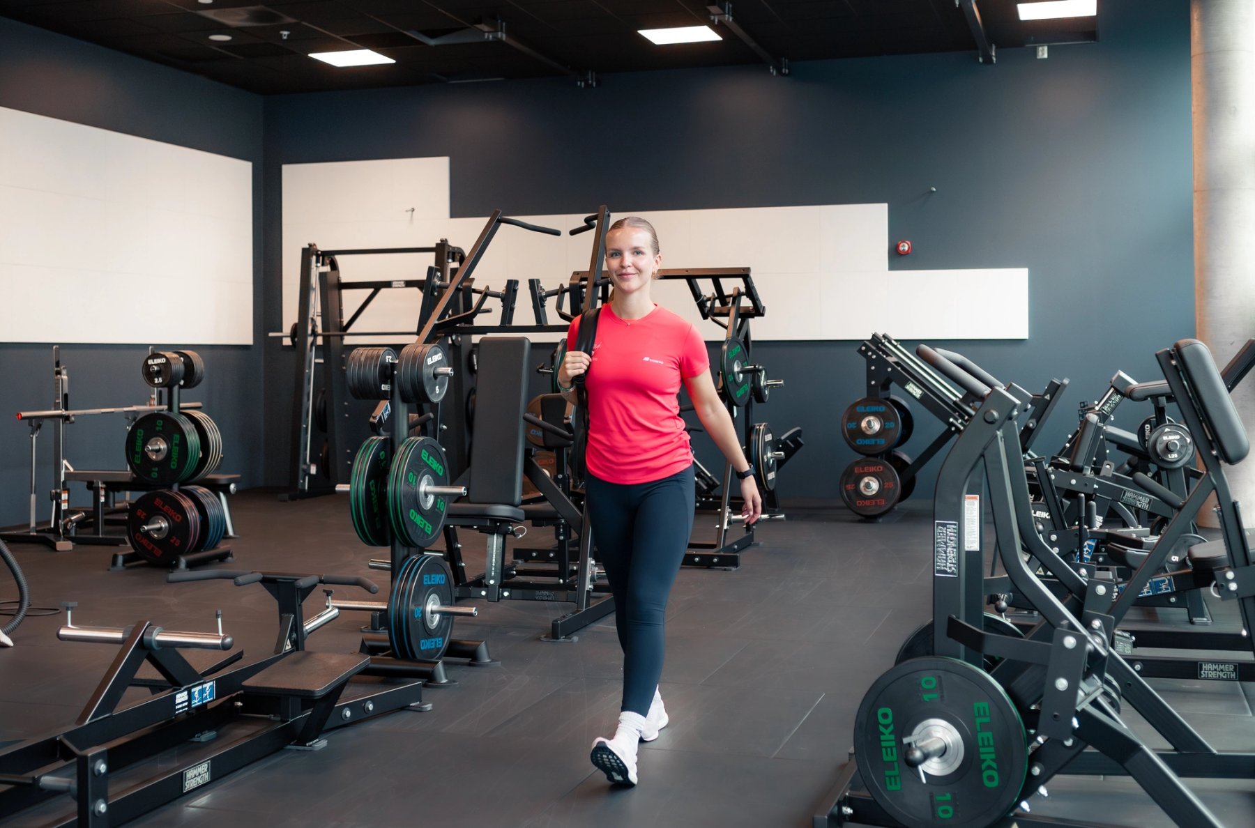 En jente som går mellom ulike styrkeapparater på et treningssenter. 