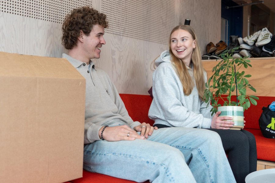 Studenter sitter i et fellesareal med flytteesker og en potteplante under innflytting.