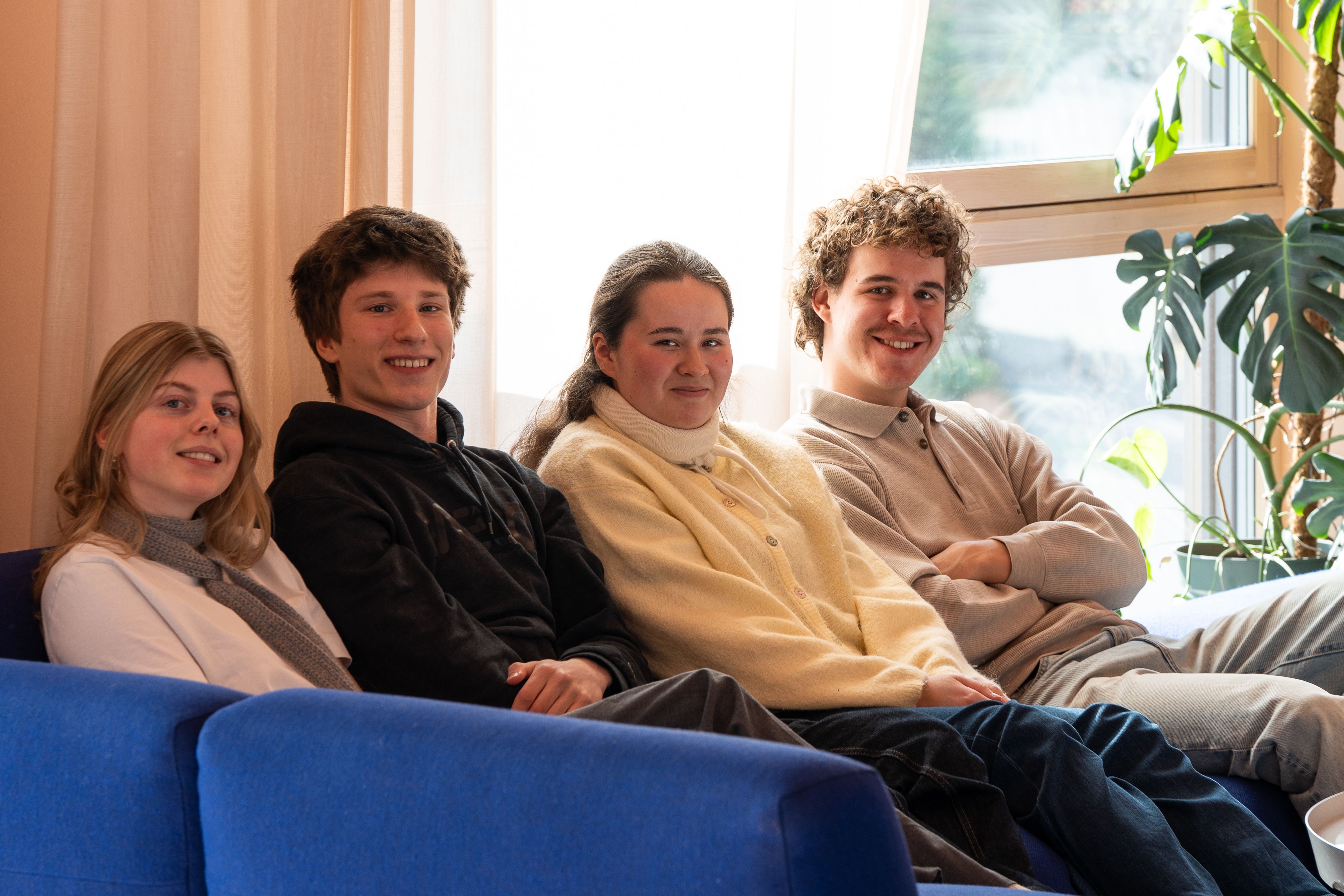 ire studenter sitter sammen i sofa i et lyst fellesområde i studentbolig.