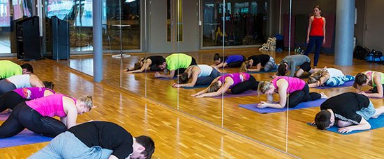 Personer i fargerik overdeler ligger foroverlent på matte, med ene kneet bøyd under seg, og tøyer setemuskulaturen. 