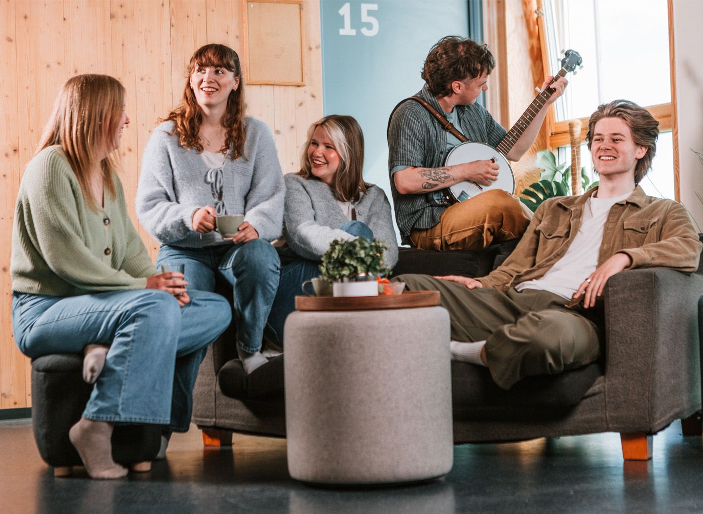 Flere studenter sitter sammen i en sofa i et felles oppholdsrom og spiller brettspill rundt et bord.