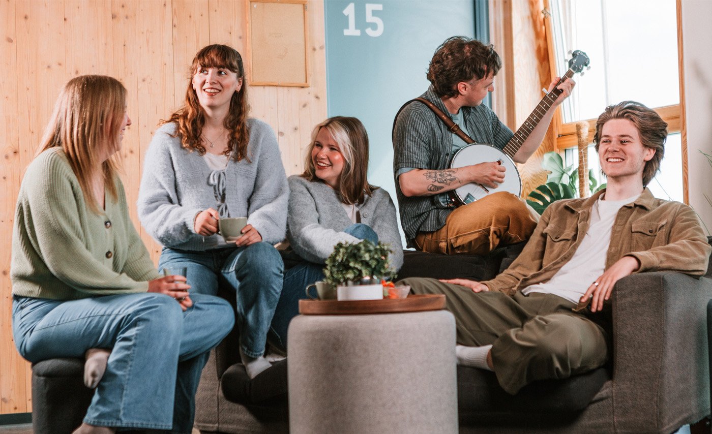 Flere studenter sitter sammen i en sofa i et felles oppholdsrom og spiller brettspill rundt et bord.