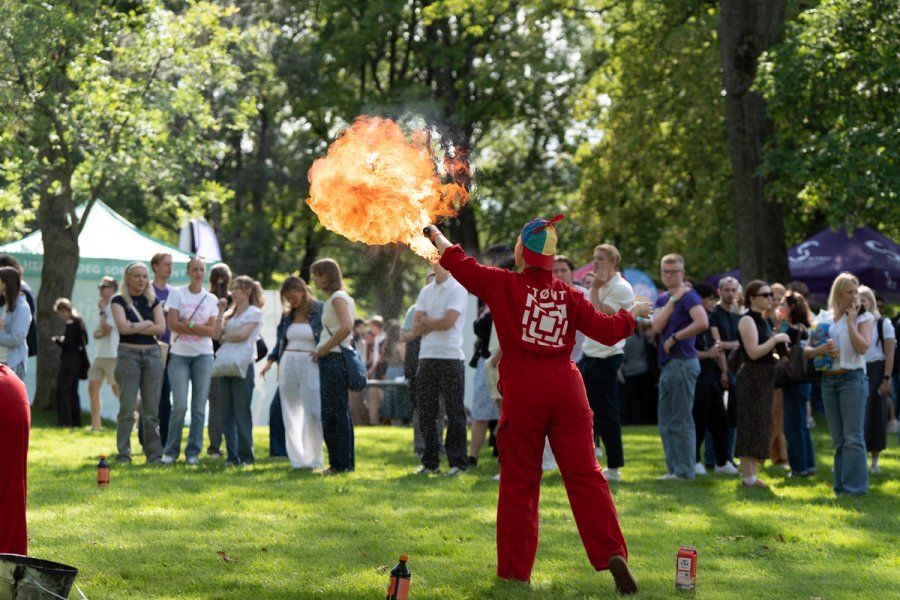 En person i rød drakt utfører ildshow foran en gruppe studenter i en park.
