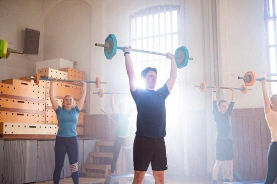 Foto av deltakere på en gruppetime der de presser en vektstang over hodet.