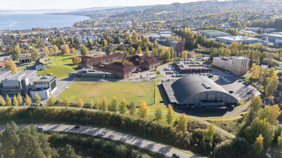 Dronefoto av Gjøvik med campusområder, bygninger og grøntarealer sett ovenfra.