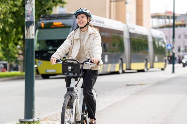 En student på en elektrisk bysykkel ved Gløshaugen i Trondheim, med en rutebuss fra AtB i bakgrunnen. 