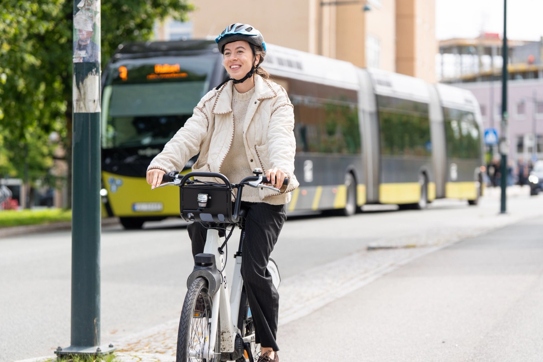 En student på en elektrisk bysykkel ved Gløshaugen i Trondheim, med en rutebuss fra AtB i bakgrunnen.