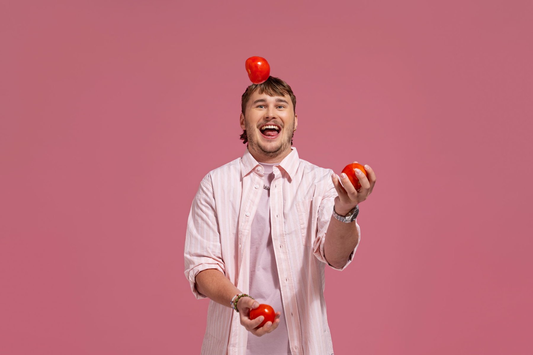 Bilde av en ung mann som sjonglerer med tomater og ser glad ut.