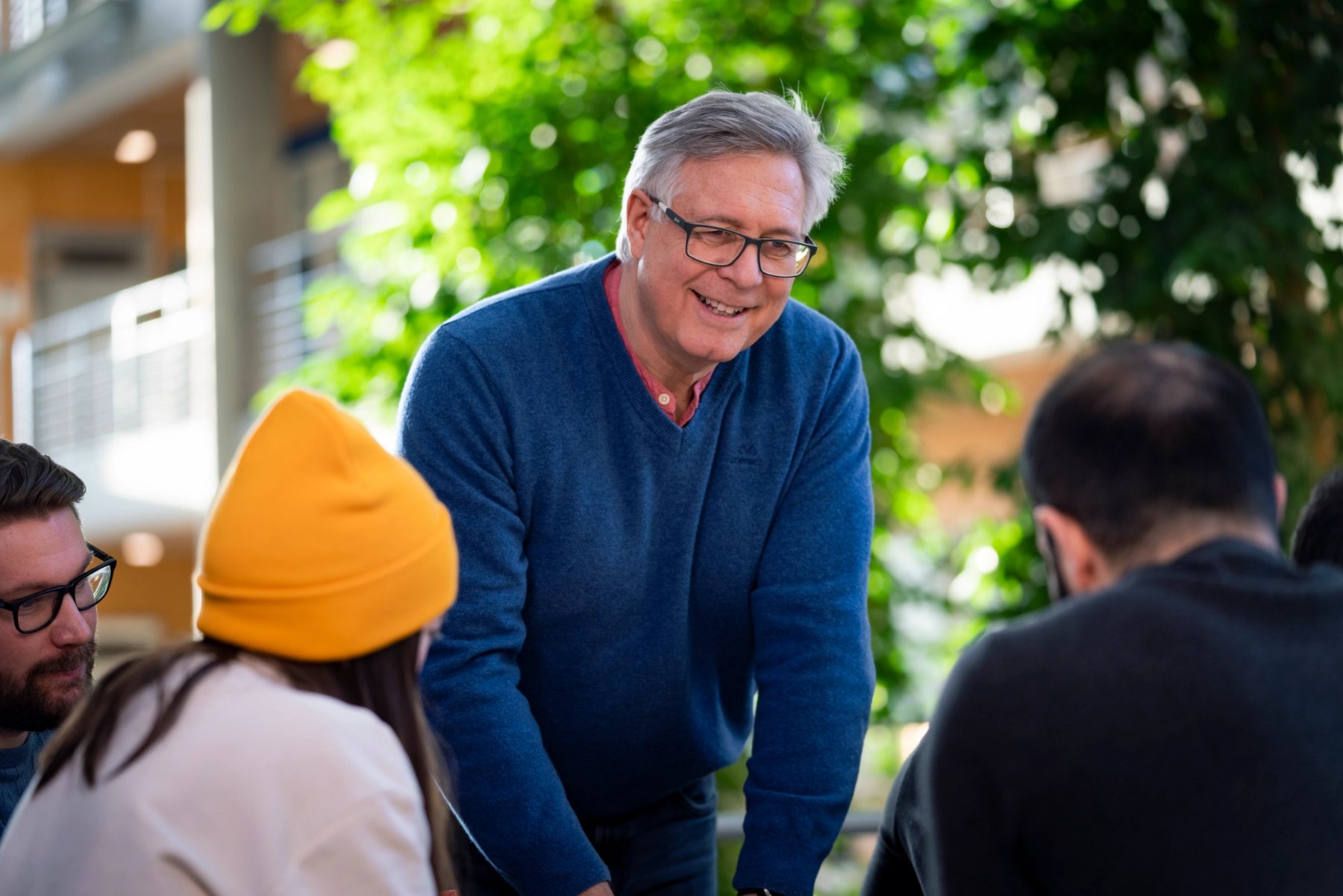 Bilde av en rådgiver som smiler og snakker med en gruppe studenter i et lyst og grønt fellesområde.