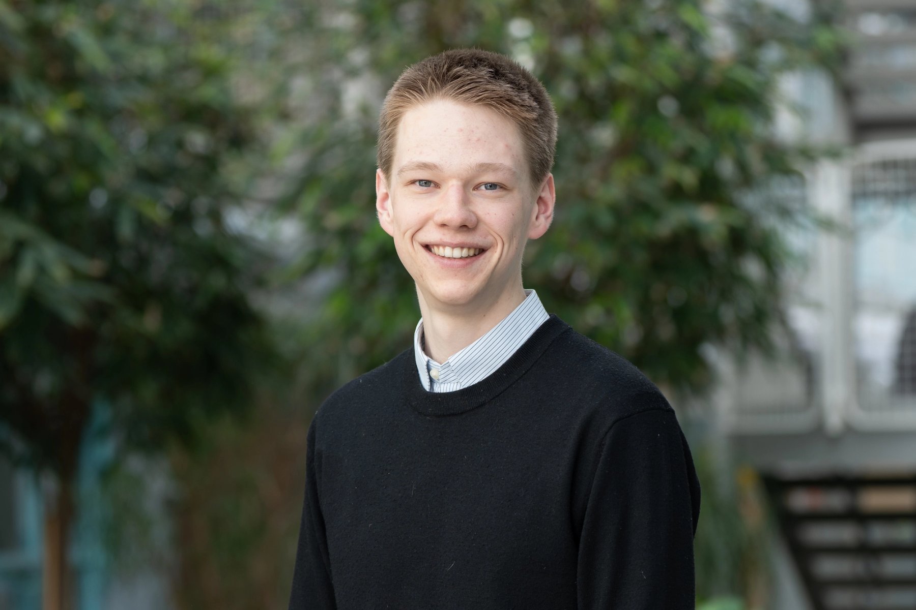 Mads Fuglesang Øhra, studentvalgt, smiler mot kamera i et grønt utemiljø.