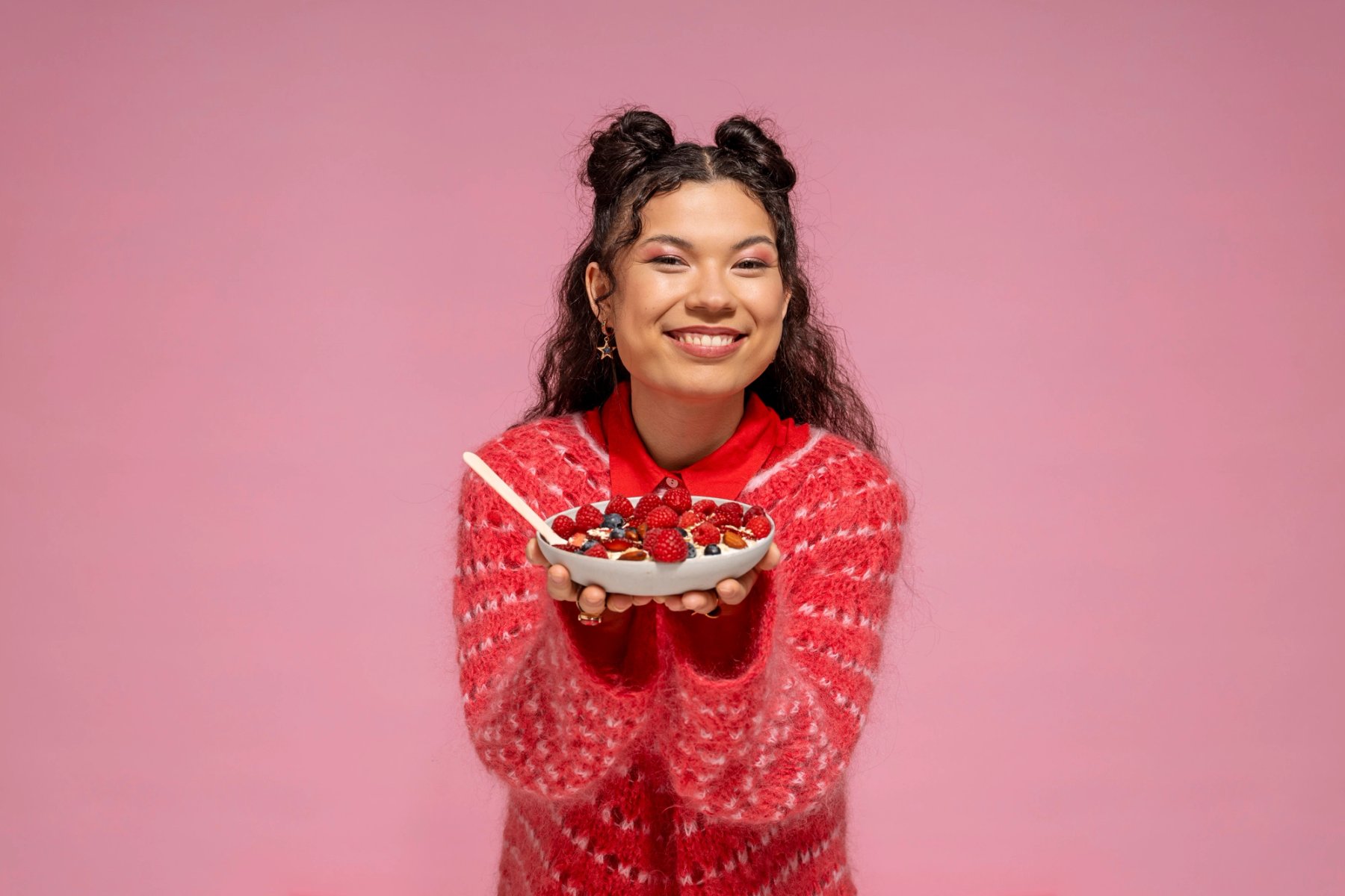 Image of a smiling student holding a bowl of porridge topped with berries and nuts, against a pink background.