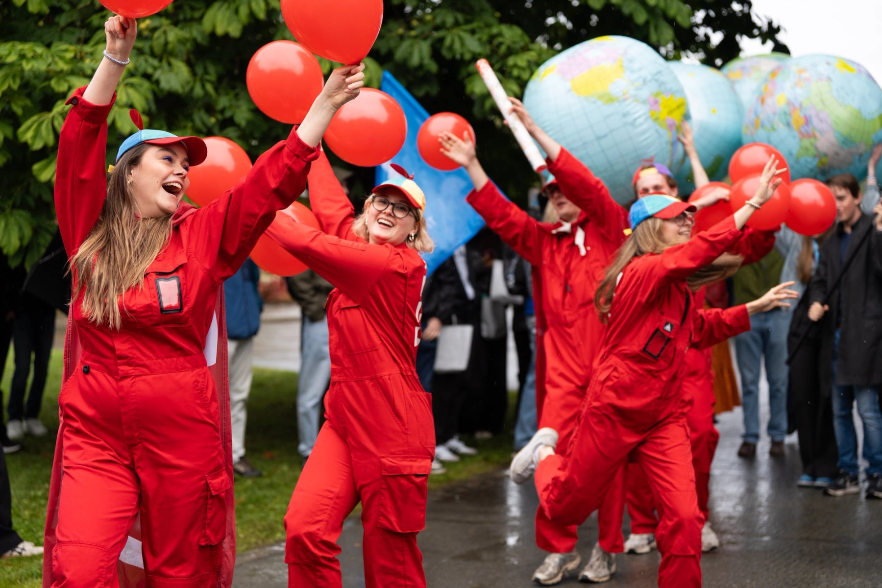 Fem studenter i rød kjeldress som vifter med ballonger.