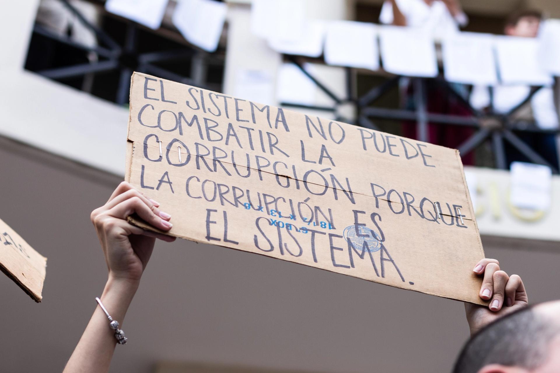 Placard in Spanish, reading 'El sistema no puede combatir corrupción porque la corrupción es el sistema'