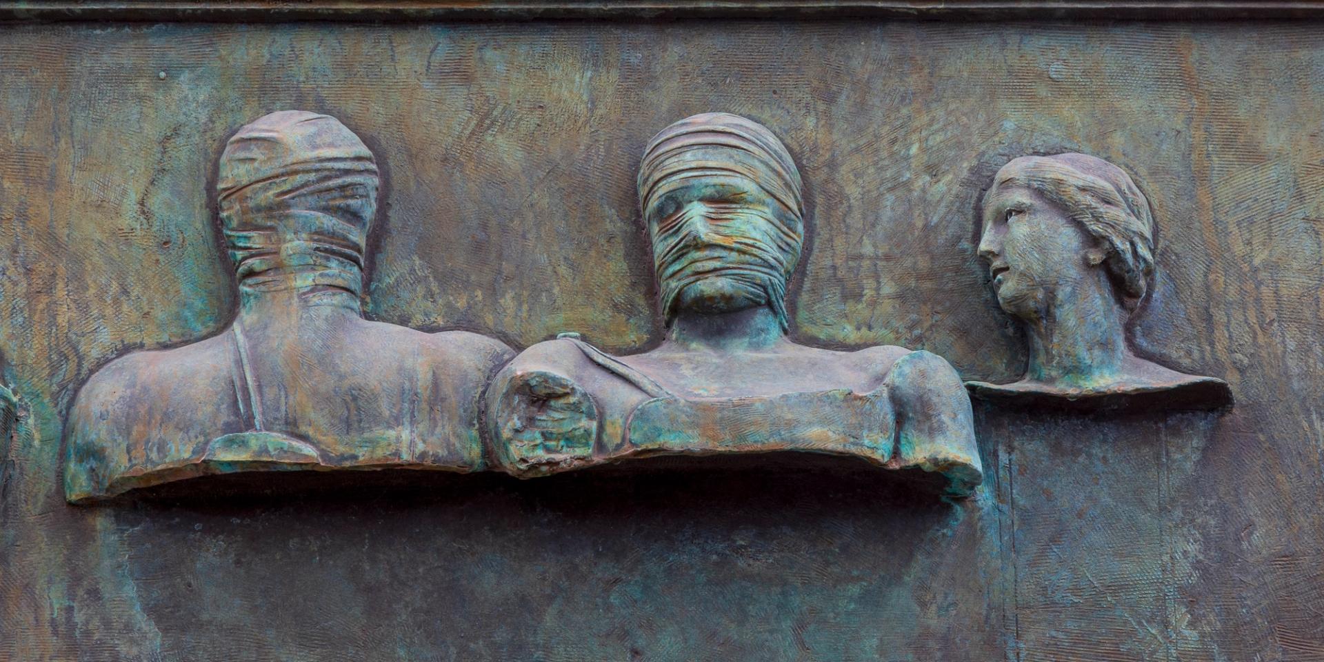 Statue showing two men with covered heads and a woman looking at them.