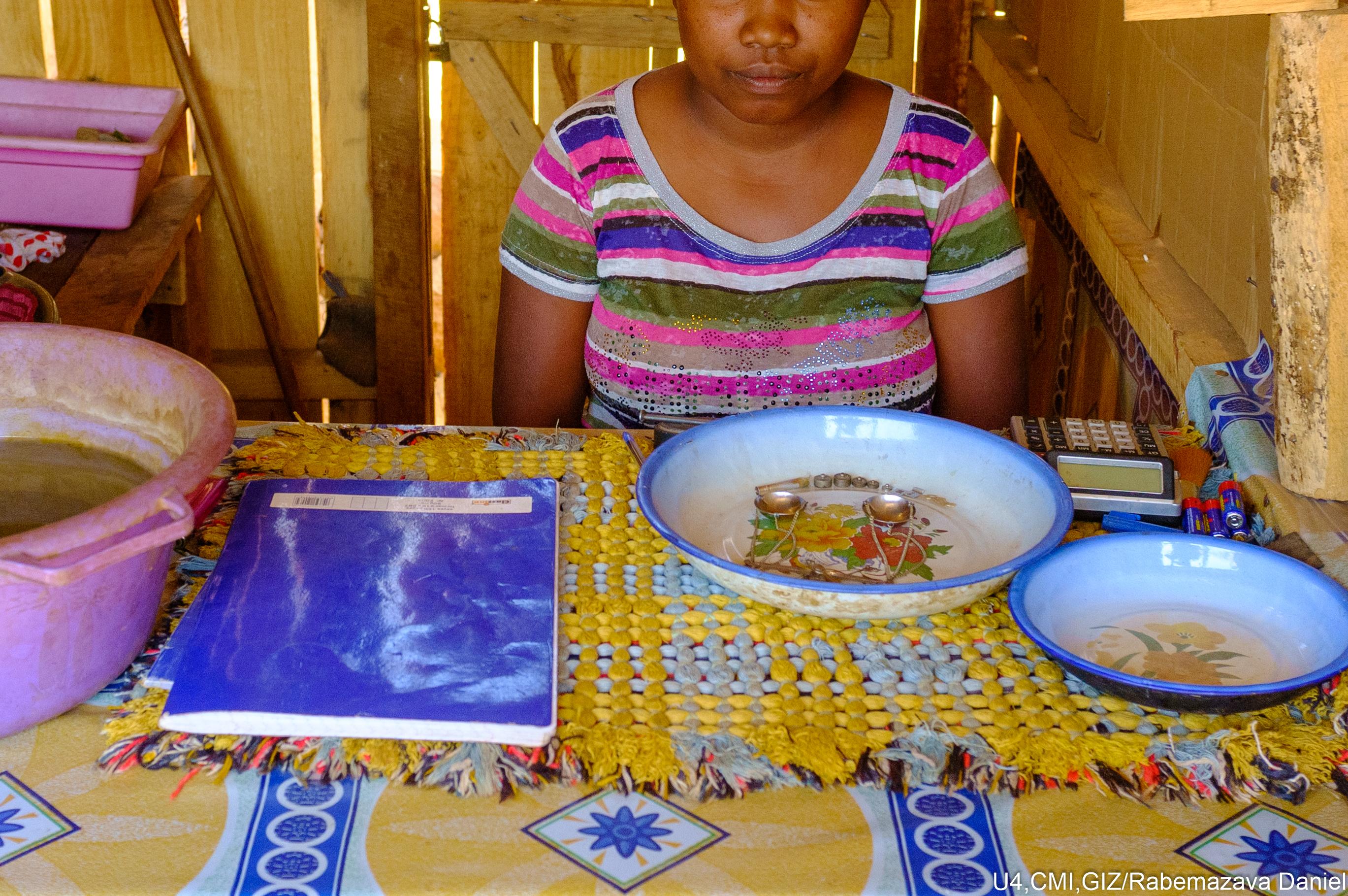 A woman at a table with a plate in front of her, containing scales for measuring gold.