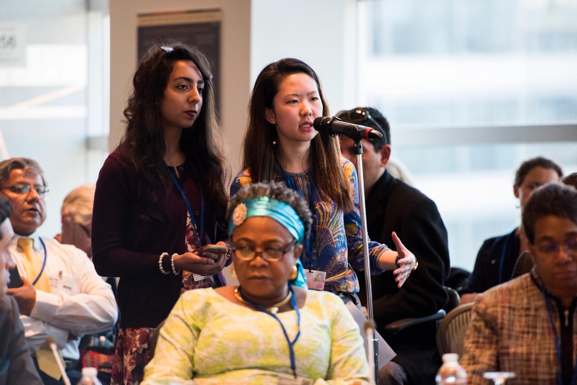 Women of diverse ethnic origin speak through a microphone at at meeting