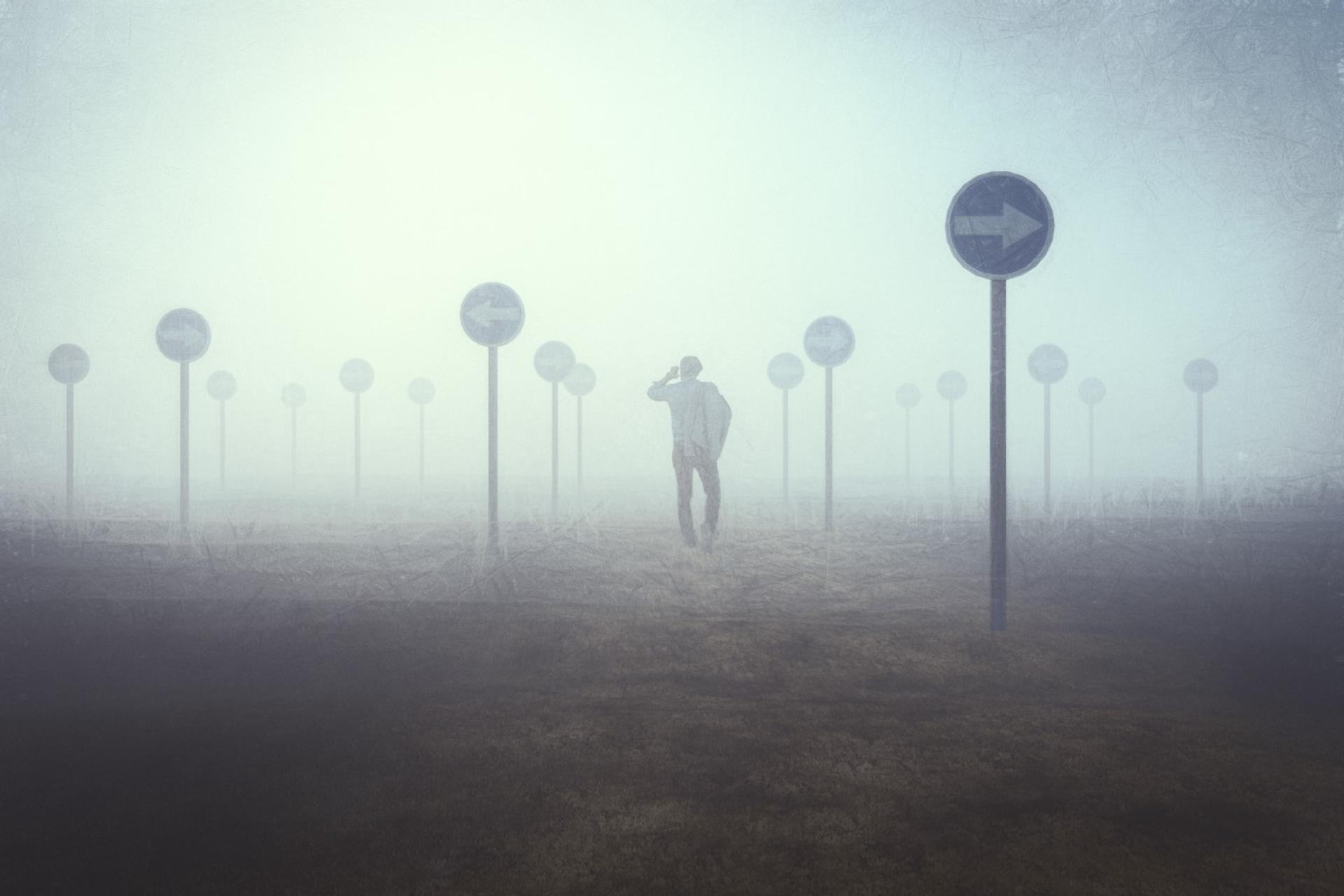 Man walking in foggy field with confusing sign-posts