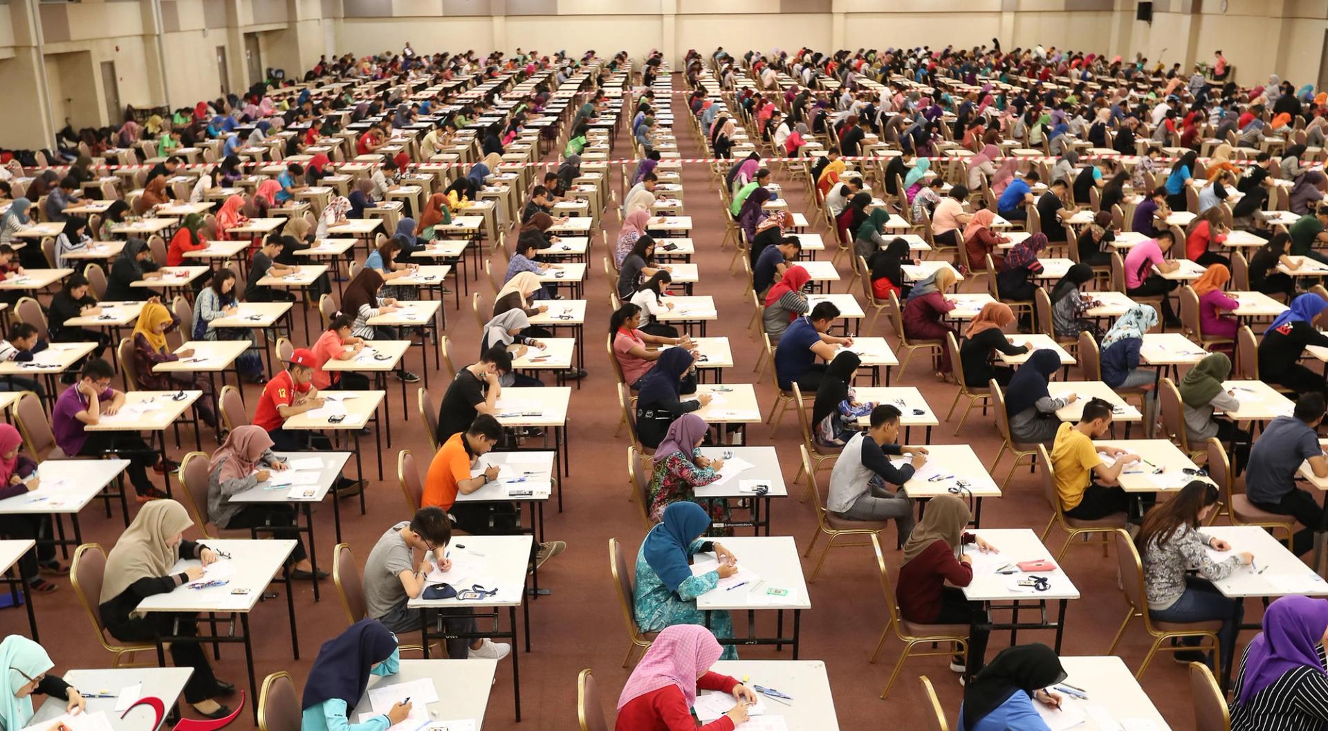Students sitting university exams in a large aula.
