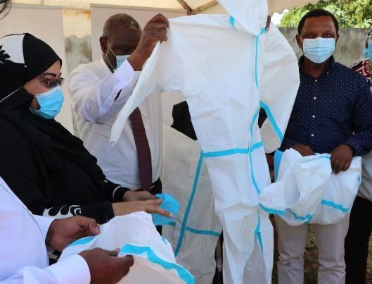 Photo of two men and one woman, all wearing surgical masks, examining plain full-body gowns or personal protective equipment.