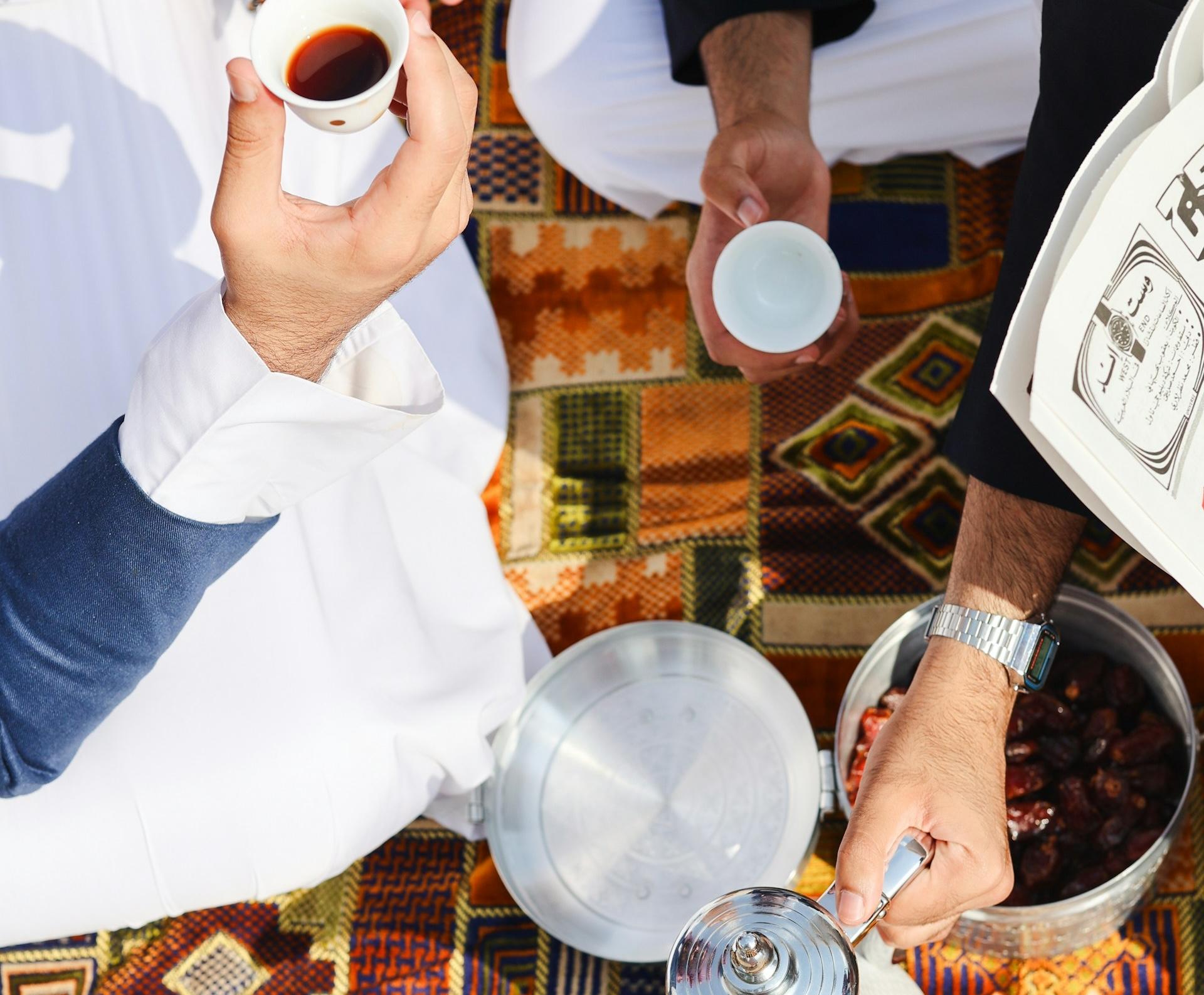 Three people sat on a picnic blanket, only their hands are visible in the image, pouring and sharing drinks