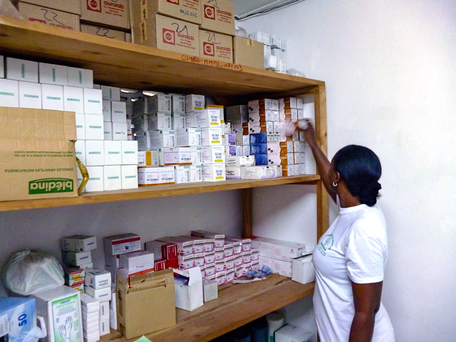A woman takes a single box of medication from a rack of shelving, full of medicine boxes.