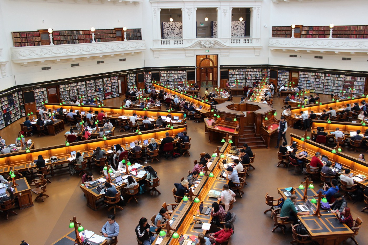 Students sit at long desks in a large, round library space, where the desks are arranged like the spokes on a wheel.