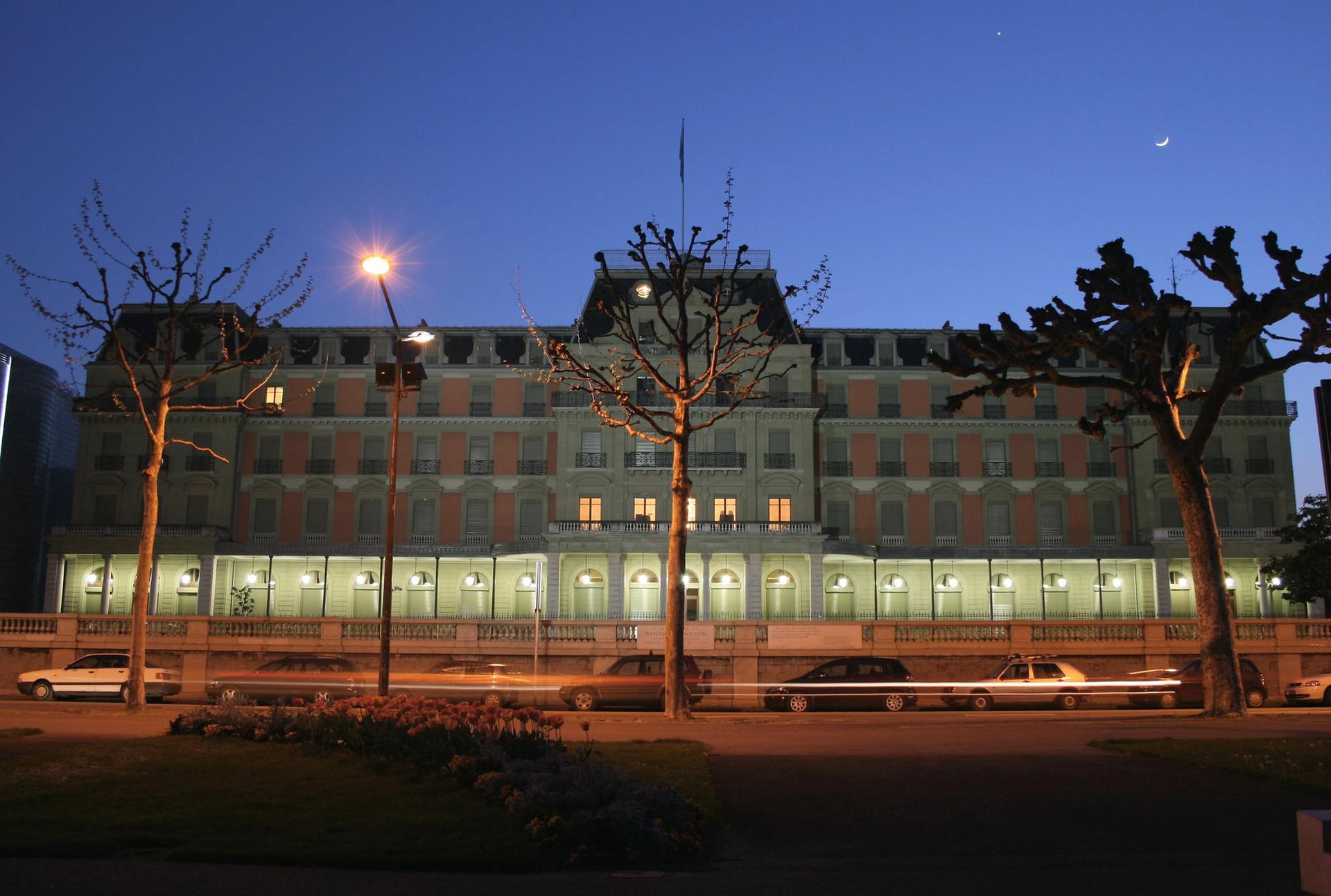 Evening photo of the Palais Wilson with darkening sky and blurred vehicle lights in the foreground.