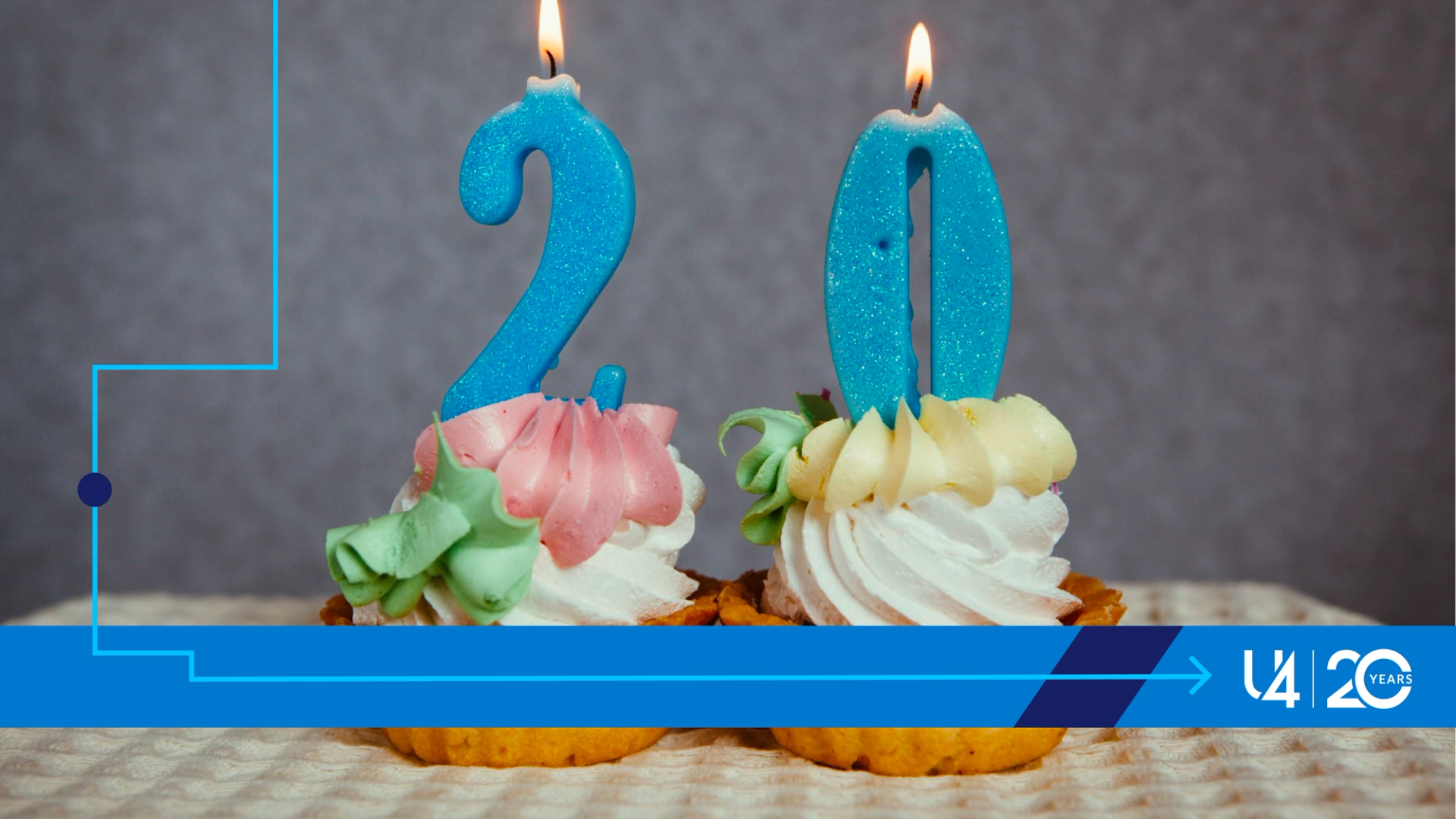Close up photo of two cupcakes, with frosting on top. Both have lit candles on top, the left one shaped like a figure 2, the right one shaped like a zero.