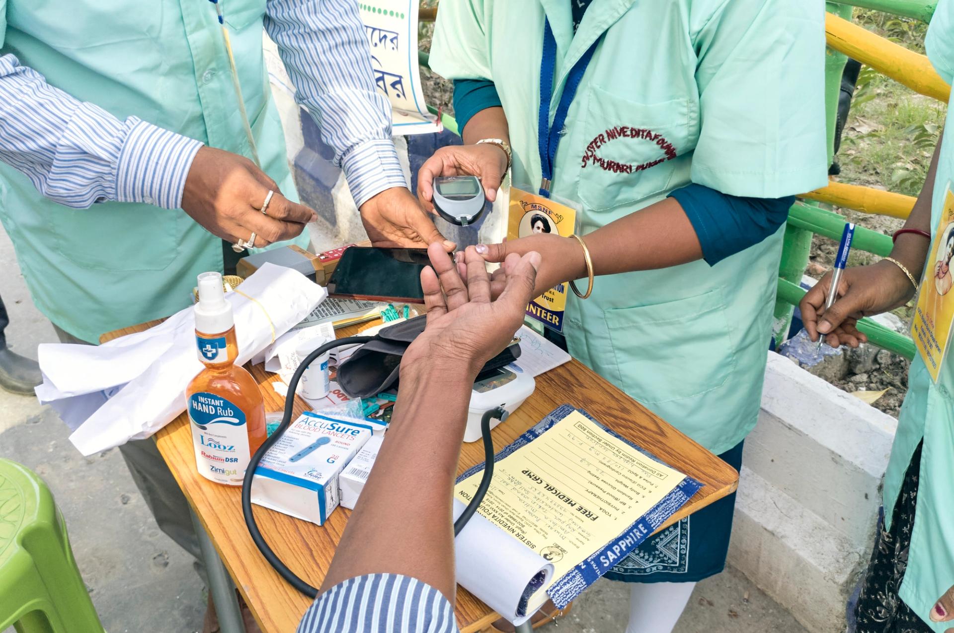 Health technicians checking blood sugar level of a person, using a digital glucometer at a roadside free health checkup camp in India.