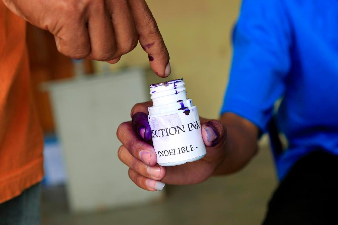 A man's finger dipping into a container of election ink