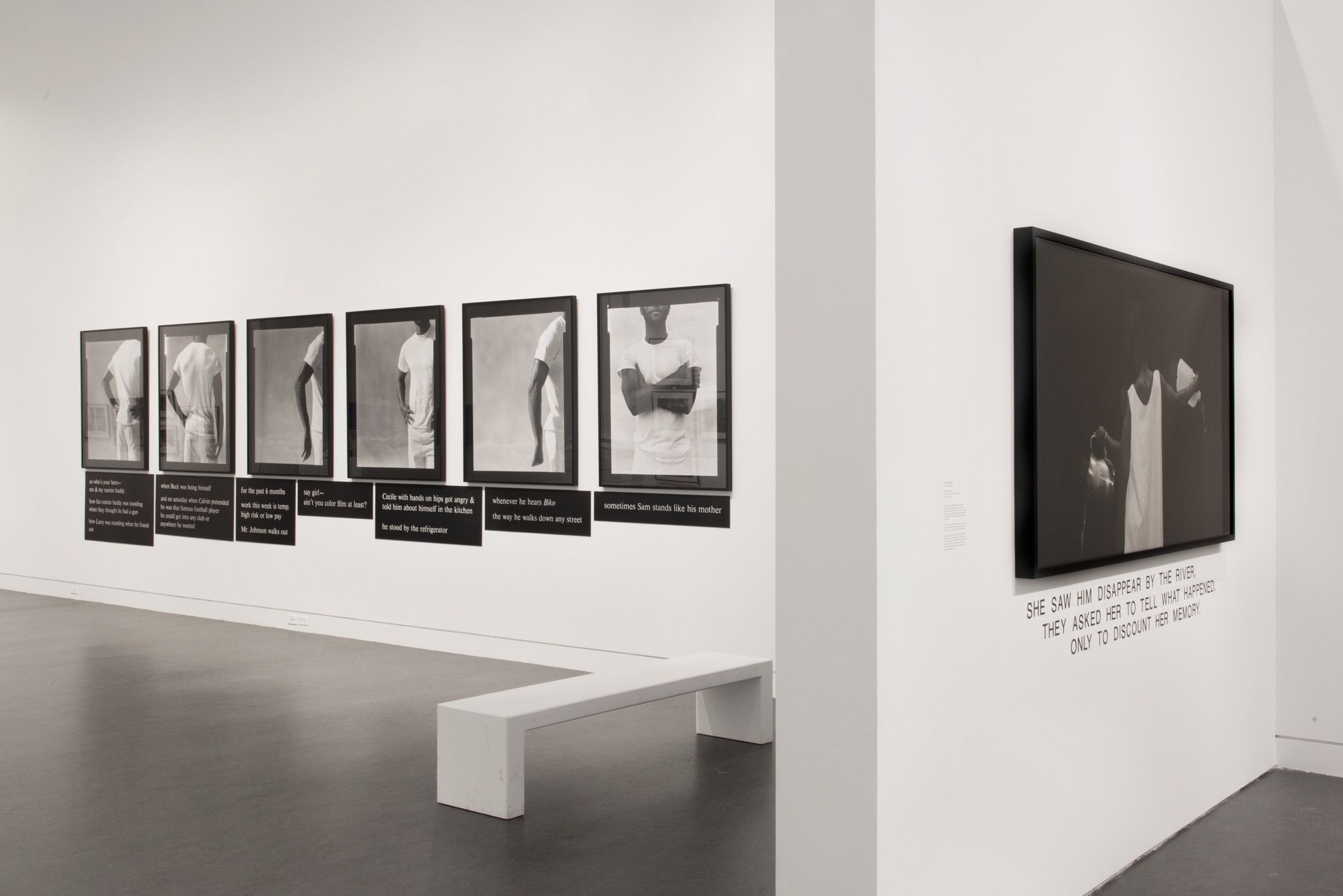 Minimalist gallery with black-and-white silhouette portraits on two walls, a white bench, and textual elements highlighting thematic narratives.