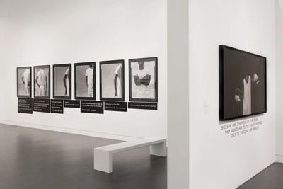 Minimalist gallery with black-and-white silhouette portraits on two walls, a white bench, and textual elements highlighting thematic narratives.