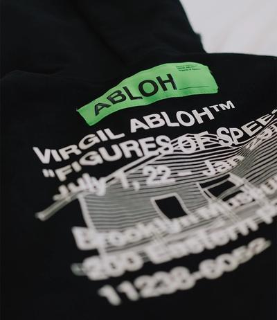 Black garment with neon green "ABLOH" and white text reading "VIRGIL ABLOH™ FIGURES OF SPEE" against plain white background, featuring blurred dates "July 7, 22 – Jan" and building-like graphic with windows, faint additional text and numbers at base.