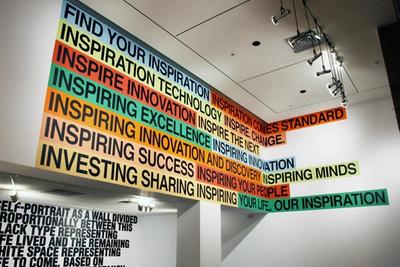 Colorful text strips on a white wall and ceiling, reading "FIND YOUR INSPIRATION", "INSPIRE INNOVATION", etc.