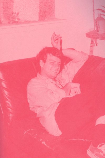 Man reclines on a leather couch, smiling, with one arm behind his head.