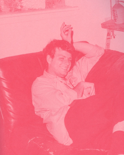 Man reclines on a leather couch, smiling, with one arm behind his head.