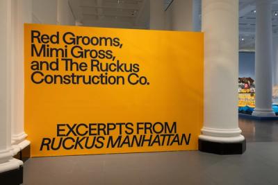 Yellow museum sign: "Red Grooms, Mimi Gross, and The Ruckus Construction Co. Excerpts from Ruckus Manhattan" amid white columns.