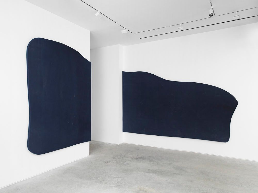 Two large, dark blue abstract shapes mounted on white walls in a minimalist gallery.